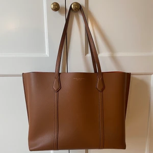 Handväska från Tory Burch - Brun handväska i läder från Tory Burch. Modellen heter ”Perry Triple-Compartment Tote”. Har ett innerfack med plats för laptop om 13 tum. Måtten är 41 x 29 x 12 (cm). Använd fåtal gånger och ser helt ny ut. Nypris 515€ (5549kr) på hemsidan. Mitt pris 2800