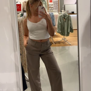 Vida kostymbyxor - Beiga vida kostymbyxor med knapp och ”hake”. Fickor och resår i midjan baktill från VILA