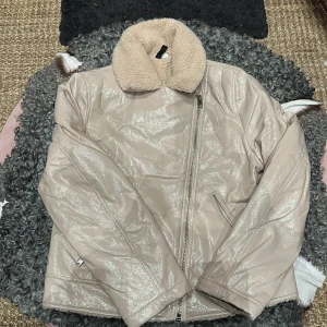 Pilefodrad bikerjacka -  En pilefodrad bikerjacka i lackad läderimitation. Jackan har krage och slag samt snedställd dragkedja fram. Sidfickor med dragkedja.