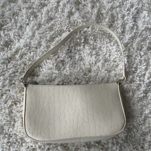 Vit axel väska - Jag säljer min vita axel väska med snygga detaljer ifrån DIVIDED (hm). Väskan har använts ett få tal gånger och är i ett väldigt fint skick. Pris kan diskuteras och om du har några frågor är det bara att höra av dig.💗