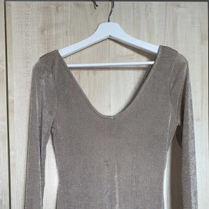 Figursydd klänning- oanvänd - Oanvänd klänning från Nelly i strl M. Tight passform i beige/glittrig färg med guldig underton