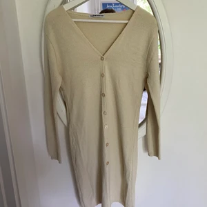 Ljusbeige stickad klänning  - Tuntstickad klänning med långa ärmar! knappar framtill! För liten för mig som bär L men tror denna passar perfekt på en S/M! Köparen står för frakt/möts i Stockholm 