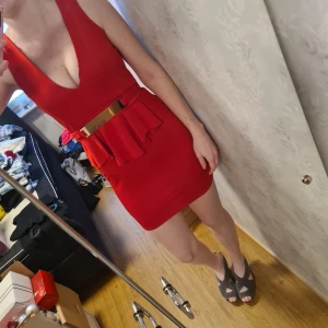 Röd klänning med fina detaljer - En röd klänning med en volang midja och guldspänne. Väldigt fin och åtsittande passform. Jag är 176cm lång och är mellan S och M i storlek. Använd ett fåtal gånger och inga skador på den alls. 