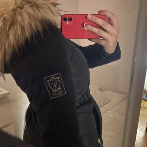 Svart jacka med päls  - Svart jacka med skärp i midjan och päls på luvan. (Kan bäras utan skärp) Märke: Chiara Forthi Nypris: 2000 Använd Max 10ggr. Kan mötas upp i sthlm,gbg,Södertälje, Kalmar. 