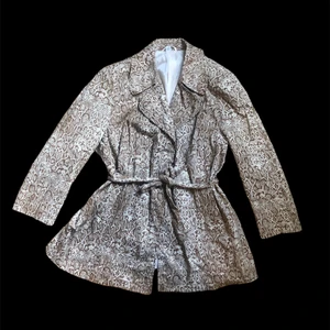 Jacka i ormskinnsprint - Trenchjacka i ormskinnsmönster 🐍 Nyskick! Storlek 48, men för mig som är en 38 sitter den även snyggt oversize.   97% bomull 3% elestan beige/brun   Med sidfickor, knytskärp i midjan, extra knappar medföljer.  