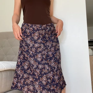 blommig kjol - blommig kjol med mörkblå, lila, bruna och gröna detaljer.  knapp framtill.  Superfin till hösten.  bara aldrig bära den, den sitter för lågt på mig.  storlek medium, skulle passa storlek small lite lägre i midjan.s