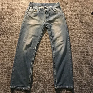 True Religion Jeans - Ett par True Religion jeans i mycket bra vintage skick förutom att lite av outline stitchingen gått upp! Storlek 32 passar folk runt 1,70cm. Kontakta mig vid frågor, fler bilder eller intresse! Tar INGA Köp Via KÖP NU funktionen.