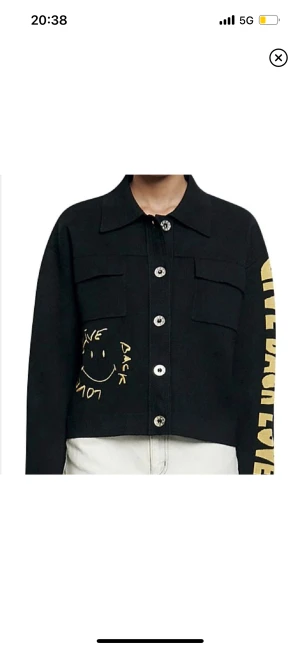 Sandro jacka - Säljer denna coola jacka/overshirt från Sandro. Jackan är knappt använd, utan i nyskick och har smiley motiv i gult, både fram och bak, samt text på vänster ärm. Första bilden är lånad! Nypris ca 4 000 SEK🫶
