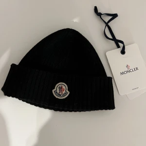 Moncler mössa  - Säljer min moncler mössa som är sparsamt använd 8/10.Dock ett håll som är ihopsytt som man inte kan se. Mössan är köpt på Man of kind för 1900kr
