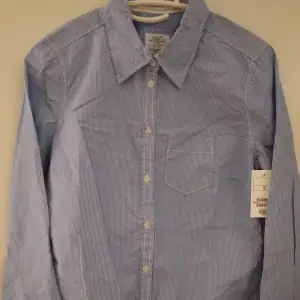 Helt NY & OANVÄND fin klassisk blå-vit smalrandig Oxford-blus/skjorta från LOGG-avdelningen/H&M. Storlek: 34/XS-S. Material: Bomull. Helt felfri. Lappar/etiketter sitter kvar sedan inköpet. Nypris i butik är 199 kr.