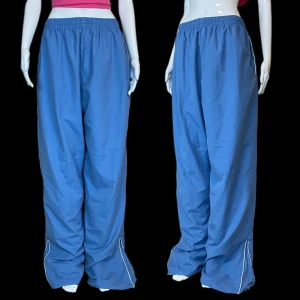 Baggybyxor  - Baggy träningsbyxor med snören. Går att zippa upp och ner dragkedjan längst ner. Stretchband. Mer ljusblåa i verkligheten! Ungefär som på sista bilden. Från märket Superpros, storlek XXL. Mått: Midjebredd 37cm, grendjup 37cm, innerbenslängd 82cm