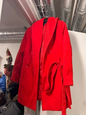 Röd kappa  - Röd kappa med luva. Lite teasig i innerfodret på höger arm men inget som förstör eller syns vid användning