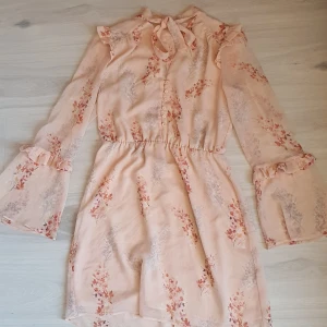 Aprikosfärgad chiffong kläning Mango stl M - Nyskick! Söt klänning med knyt i hals, knappar fram, trumpetärm. Resår i midjan Stl M ca 40  Skickar spårbart. Tryck köp direkt  Har inga bilder där den är på.  Mvh