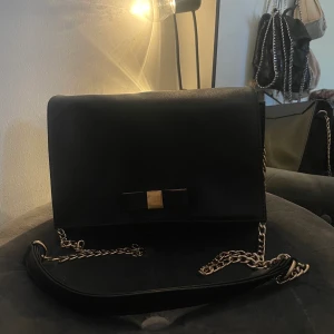 Svart väska med rosett  - Säljer denna svarta väskan med rosett. Man kan antingen ha den som en axelbands väska eller så kan man snurra in kedjan i väskan så kedjan blir mindre så kan man använda den enkelt på axeln. Hör av dig vid frågor eller mer bilder!☺️🙌🏼
