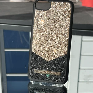 Ett svart och guldigt glittrigt skal. - Ett svart och guld glittrigt skal som passar din Phone som är en 6, 7, 8. Säljer skalet pga av byte av telefon.