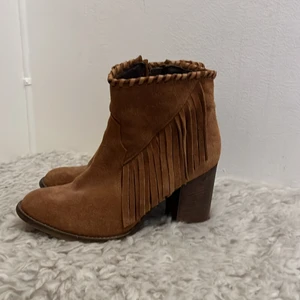 Mockastövletter i congac med fransar - Congacsbruna klackskor i mocka, fransar på utsidan, deltaljsöm med läder upptill. Dragkedja för att stänga. Klackhöjd ca 8cm. 