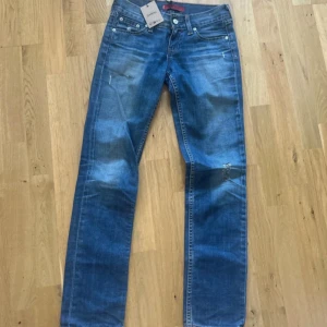 Blå jeans från Levi's - Säljer ett par snygga blå lågmidjade jeans från Levi's. De är i en klassisk straight fit och har en cool, sliten look med några små revor. Märket är Levi's, vilket garanterar bra kvalitet och hållbarhet. Passar perfekt till vardags!