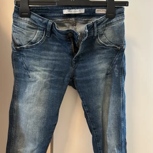 Jeans dam - Jeans med unik modell där det finns en dragkedja på sidan också. Finns lite slitningar som tillhör modellen. Slimfit. Storlek 26/32.