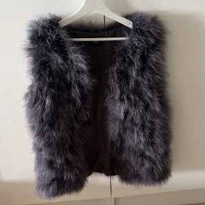 Grå pälsväst från H&M - Säljer en supermysig grå pälsväst från WOS. Den är perfekt för höst och vinter och ger en lyxig känsla till vilken outfit som helst. Västen är i nyskick och har en normal passform. Perfekt för både vardag och fest!