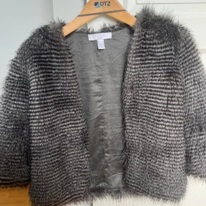 Grå pälsjacka från NA-KD - Säljer en superfin grå pälsjacka från NA-KD. Den är perfekt för att ge din outfit en lyxig touch. Jackan har ett randigt mönster och trekvartsärmar, vilket gör den både trendig och bekväm. Perfekt för höst och vinter!