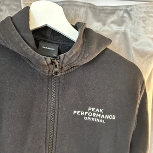 Peak Performance Luvtröja - Svart Peak Performance luvtröja i storlek 170 (barnstorlek). Tröjan är köpt på Kids Brand Store och är äkta. Den är väl använd och därmed lite urtvättad. Annars fint skick, inga hål eller fläckar.