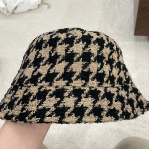 Beige och svart rutig hatt - Säljer en supercool beige och svart rutig hatt i ett klassiskt mönster. Perfekt för att ge din outfit en trendig touch. Hatten är mjuk och bekväm, idealisk för både höst och vår. Passar de flesta huvudstorlekar.
