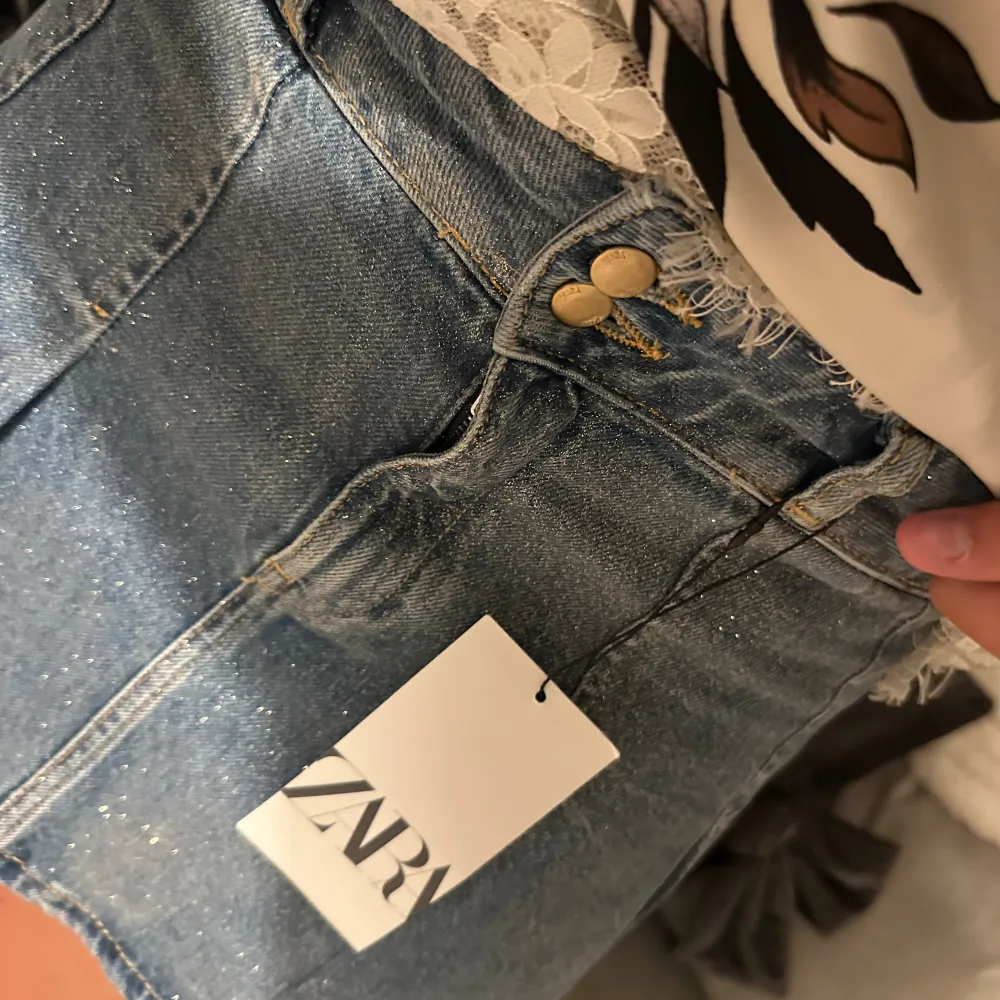 Säljer en superfin jeanskjol från Zara! Den är kort och har en snygg A-linjeform som ger en skön passform. Kjolen har två knappar fram och är i ett klassiskt blått denimtyg. Perfekt för både vardag och fest! Glitter över hela. Oanvänd med lappar kvar. Storleken är M men passar S också. Kjolar.