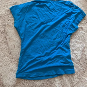 Blå topp med öppen rygg - Säljer en snygg blå topp med öppen rygg. Perfekt för sommaren och festliga tillfällen. Toppen är ärmlös och har en tight passform. Materialet är mjukt och bekvämt, troligtvis bomull eller en bomullsblandning. Passar perfekt till både jeans och kjol!