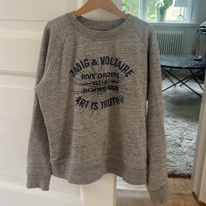 Collage tröja från Zadig & Voltaire - En jättefin collage tröja från Zadig & Voltaire med tryck på framsidan. Det står namnet i marinblått med stenar och tröjan är grå. Jätteskön och snygg! Köparen står också för frakt.