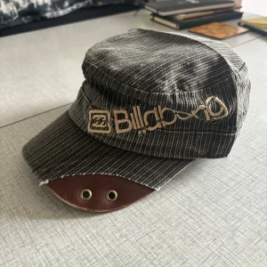 Vintage Billabong manchestertyg gråbrun keps - En snygg keps i Manchestertyg och gråbrun färg med Billabong-logotypen på framsidan. Kepsen har en läderlapp på skärmen och en justerbar rem i baken med två knappar. I fint skick!