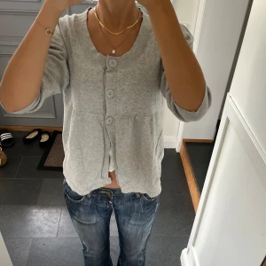 Grå stickad volangkofta - Grå trekvartsärmad stickad kofta med knappar och volanger. Storlek M, passar även S. Fint skick. Använd gärna köp nu!