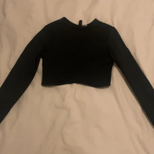 Svart croppad topp från H&M Divided - Säljer en svart croppad topp från H&M Divided. Den är långärmad och perfekt för en trendig look. Toppen är i bra skick och passar utmärkt till både vardag och fest.