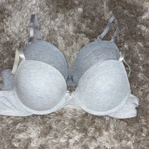 Grå spets-bh från Censored - Säljer två gråa bh-ar från new yorker med spetsdetaljer. Den har justerbara axelband och en bekväm passform. Perfekt för vardagsbruk eller speciella tillfällen.