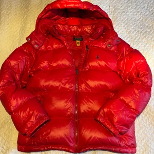 Polo Ralph Lauren puffer jacket  - Snygg röd dunjacka från Polo Ralph Lauren med huva och dragkedja.🙌 |||Jackan har en glansig finish och är perfekt för kyligare väder🥶. Den har långa ärmar och två praktiska fickor och en dragkedja. Den har inga som helst diffekter förutom att hängaren är av och den är lite fläckig på armarna skriv om ni vill bild||| Nypriset runt 5500kr 💸mitt pris 2450kr 💸priset kan diskuteras🙌skriv vid minsta fundering 💭 