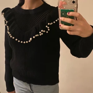 Svart stickad tröja med pärldetaljer - Snygg svart stickad tröja med pärldetaljer och lite mellanrum genom tyget vid bröst delen. Är ganska ny och sitter ganska bra. Mina bilder !!