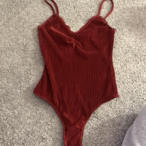 Röd ribbad bodysuit från BikBok - Snygg röd bodysuit från BikBok i storlek XS. Den har smala axelband och ett ribbat mönster som ger en stilren look. Perfekt för att styla med jeans eller kjol.