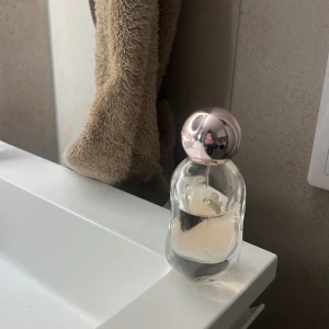 Cosmic Eau de Parfum av Kylie Jenner - Elegant parfymflaska med en mjukt rundad form och en stilren design. Flaskan är genomskinlig med en ljusrosa kork som ger en lyxig känsla. Perfekt för den som vill ha en doft med en touch av glamour.