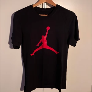Svart t-shirt med röd Jordan-logga - Snygg svart t-shirt från Jordan med den ikoniska röda loggan på framsidan. Kortärmad och bekväm passform. Storlek XS men är lite oversized så kan passa S också. Använd några få gånger.