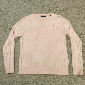 Ljusrosa stickad tröja från Gant - Säljer en ljusrosa kabelstickad tröja från Gant.  Den har Gants loggan på bröstet. Använd men i bra skick, finns några små fläckar men inget som syns mycket.💕