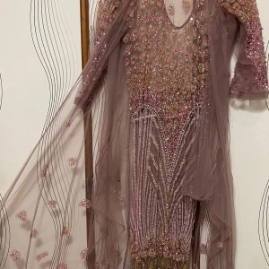 Rosa glittrig klänning med pärlor - Elegant rosa klänning med glittriga detaljer och pärlor. Den har en v-ringad design och långa ärmar. Klänningen är dekorerad med ett transparent lager som ger en extra dimension. Köpt för 2000 och är en festlig klänning 