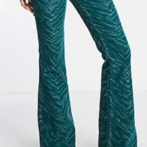 Gröna zebra-mönstrade byxor - Snygga gröna byxor med zebra-mönster och bootcut-stil. Perfekta för att sticka ut med en unik look. As balla men lite små för mig ganska låga i midjan och långa men går att klippa av skriv till mig för fler bilder. De är strl S men lite stretch i så de funkar för en M också