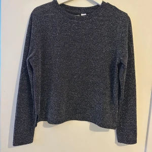 Svart glittrig tröja från Divided - Snygg svart tröja från Divided med glittrigt mönster. Tröjan har långa ärmar och en rund halsringning.