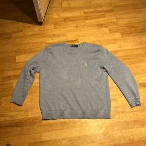 Ljus blå från Polo Ralph Lauren - Säljer en stilren ljus blåtröja från Polo Ralph Lauren med det klassiska gula logotypbroderiet på bröstet. Tröjan har en rund halsringning och ribbade muddar vid ärmslut och nederkant. Perfekt för en avslappnad och snygg look. Säljer pga den är för stor
