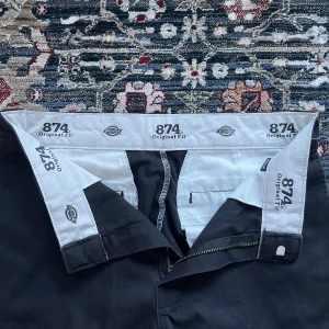 Svarta kostymbyxor dickies! - Säljer ett par klassiska svarta Dickies 874 Original Fit byxor. De har en rak passform och är tillverkade i slitstarkt material med dragkedja och knapp framtill. Perfekta för en stilren look. Endast testade av mig, köpta på Plick, men i mycket bra skick! 