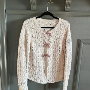 Beige stickad kofta från Odd Molly - Charmig beige stickad kofta från Odd Molly med vackert mönster och tre rosetter framtill. Koftan har långa ärmar och ett broderat märke på ärmen. Perfekt för en mysig och stilren look.