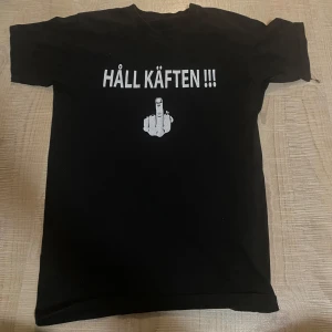 Svart t-shirt med tryck - Svart t-shirt med ett vitt tryck som säger 'HÅLL KÄFTEN !!!' och en bild av en hand som visar långfingret.
