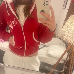 Röd hoodie från billabong - Säljer en snygg röd hoodie med dragkedja och vita detaljer. Den har en mysig fodrad insida och mönster på ärmarna. Perfekt för en avslappnad stil. Står inte storlek men uppskattar till S/M