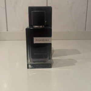 Yves Saint Laurent parfym - Elegant parfym från Yves Saint Laurent i en stilren flaska med svart lock. Flaskan har en modern design med en mörk toning som övergår till klar glas. Perfekt för den som söker en sofistikerad doftupplevelse. Är ungefär 90ml kvar i flaskan. 