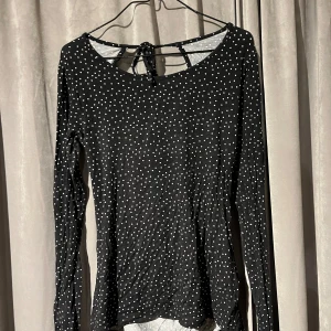Svart prickig topp från Cubus - Snygg svart topp från Cubus med vita prickar och en öppen ryggdetalj. Toppen har långa ärmar och en knytning i ryggen som ger en extra touch. Perfekt för en stilren look. S, använd en gång.