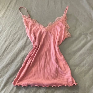 Rosa ribbad linnetopp från Amisu - Säljer en söt rosa ribbad linnetopp från Amisu med spetsdetaljer vid halsringningen. Perfekt för varma dagar eller som ett lager under en tröja. Justerbara axelband för bästa passform.